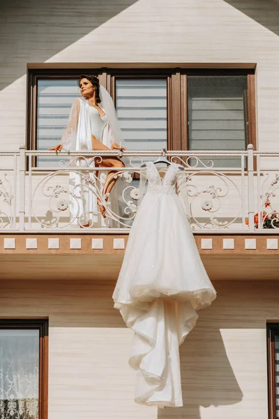 阳台栏杆上挂着白色婚纱 前面是宽阔的房子 阳台上是女孩 婚礼细节 带有长列的现代婚纱 袖子长 后背开阔 — 图库照片