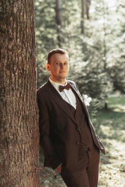 Ormandaki damadın portresi geniş açıda, damat omzunu bir ağaca dayar, fotoğraf arka plandadır..