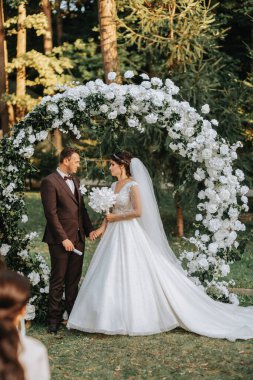 Düğün sonbahar seremonisinde güzel bir çift. Yuvarlak kemer beyaz çiçeklerle süslenmiş.