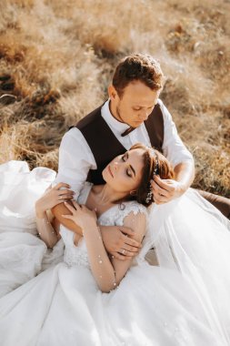 Sonbahar otlarının arka planında bir gelinle şık bir damadın portresi. Dağlarda kırsal evlilik kavramı, mutlu bohem yeni evliler. Gelin ve damat çimlerin üzerinde yatıyor.