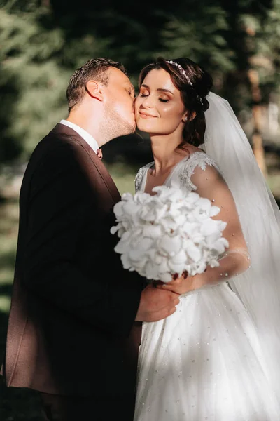 新郎轻轻地吻新娘的脸颊 他们捧着一束白兰花 — 图库照片