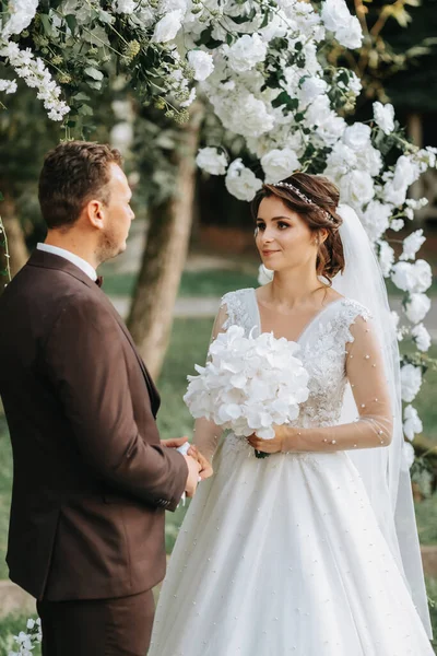 美丽的新婚夫妇在秋天的婚礼上 圆形的拱门装饰着白花 — 图库照片