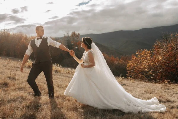 Wedding couple walks in the mountains. The groom leads the bride by the hand. The dress of the bride develops in the wind.