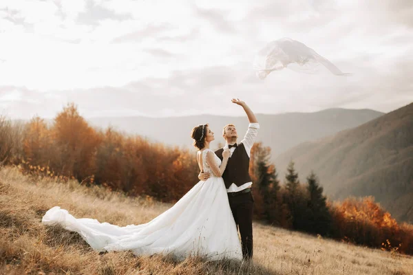 幸福的新婚夫妇在美丽的山景前摆姿势 空气中飘扬着婚纱 — 图库照片