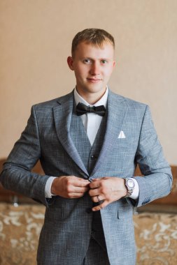 Şık bir damadın portresi sabahki düğün törenine hazırlanıyor. Damat sabahı. Damadın sabahı için hazırlık. Damat mavi ceketini bağlıyor. Büyük bir portre.