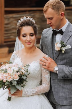 Parkta yakışıklı damat ve çekici gelin birlikte, ona bakıyor. Portre. Uzun trenli lüks bir elbise. Zarif genç damat. Düğün buketi. lüks düğün