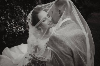 Damat ve gelin parkta. Ormanda sonbahar düğünü. Mutlu düğün, duvağın altında sevgi dolu çift dokunuşları. Şık ve güzel. Uzun trenli prenses elbisesi. Siyah beyaz fotoğraf