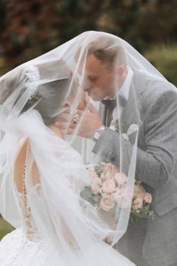 Damat ve gelin parkta. Ormanda sonbahar düğünü. Mutlu düğün, duvağın altında sevgi dolu çift dokunuşları. Şık ve güzel. Uzun trenli prenses elbisesi..