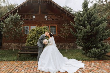 Yakışıklı damat ve çekici gelin parktaki modern ahşap evin yakınında birlikte kalıyorlar. Geniş açı fotoğraf, metin için yer