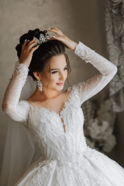 漂亮的新娘在婚礼前在家里穿好衣服 一个穿着婚纱的黑发新娘露出了她的头冠 朝窗外看去 — 图库照片