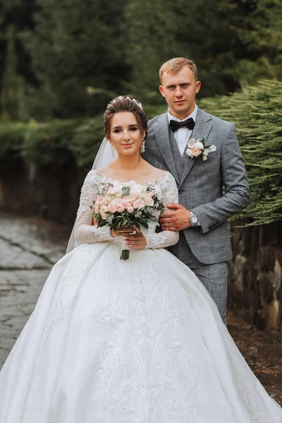 漂亮的新郎和迷人的新娘一起在公园里 带有长列火车的豪华服装 优雅的年轻新郎结婚花束 豪华婚礼 — 图库照片