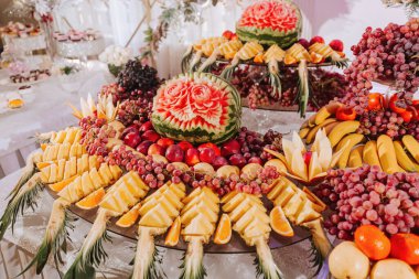 Çeşitli meyve süslemeleri olan bir masa. Karpuz oyma, ananas dilimleri, üzümler, portakal