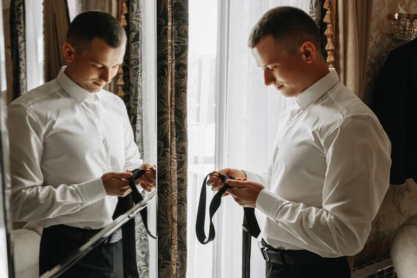 年轻人手里拿着领带在房间里 靠近酒店房间的镜子 拍了一张特写照片 新郎正在为婚礼做准备 — 图库照片