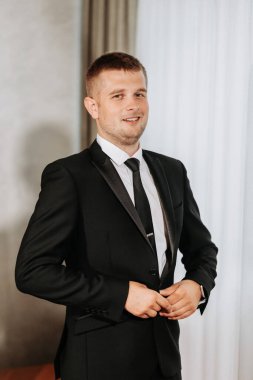 Odasında siyah ceketini ilikleyen yetişkin bir adamın portresi. Damat düğün töreni için hazırlanıyor..
