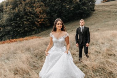 Romantik bir peri masalı çifti gün batımında eğrelti otu yapraklarının arkasında bir tarlada yürüyor. Gelin beyaz bir gelinlik, damat siyah klasik bir takım elbise ve beyaz bir gömlek giyiyor.