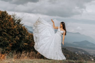 Önündeki sonbahar dağlarının arka planında güzel bir gelin. Lüks beyaz bir elbise dalgalanıyor. Dağın tepesinde düğün töreni. Boş alan.