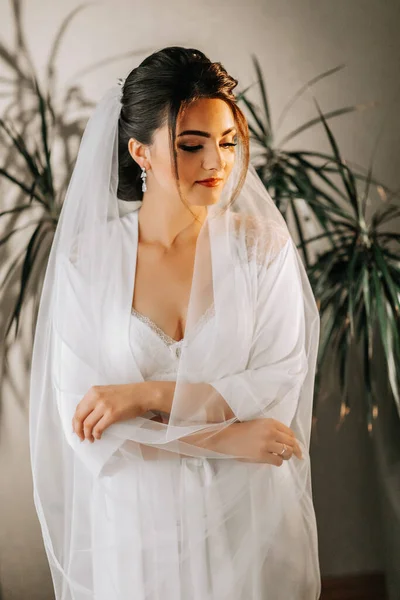 白い衣を着た花嫁の朝とエレガントな髪型 信じられない女性の化粧 結婚式のための花嫁の準備 女の子は写真家のためにポーズ — ストック写真