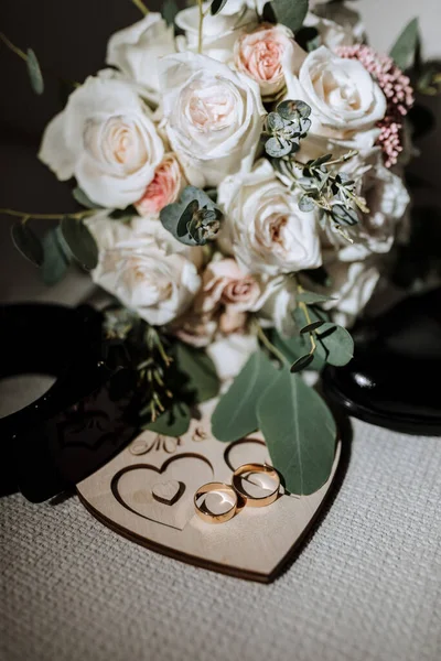details of the groom are arranged in a composition. Black shoes, wedding bouquet, gold wedding rings on a wooden stand, black men\'s belt