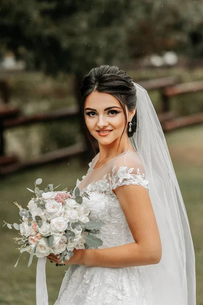 Portrait of a brunette bride in a white wedding dress with a wedding bouquet in the park. Full length photo. White lace wedding dress
