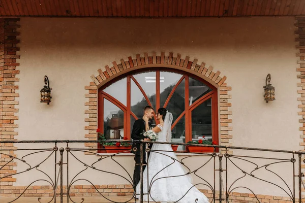 新娘和新郎的肖像映衬在一座古老而真实的房子的窗前 拥抱和亲吻 自由空间 婚礼在公园里散步 — 图库照片