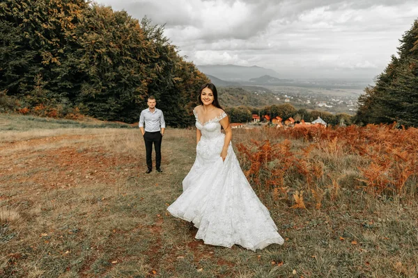 Wedding couple walking in the mountains. The bride walks to the groom looking into the camera. The bride's dress develops in the wind. Wonderful autumn weather