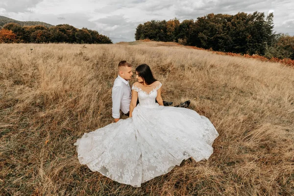 新娘和新郎躺在干枯的草地上 抱着一个穿着白色婚纱的女人 美丽的秋天婚纱照 — 图库照片