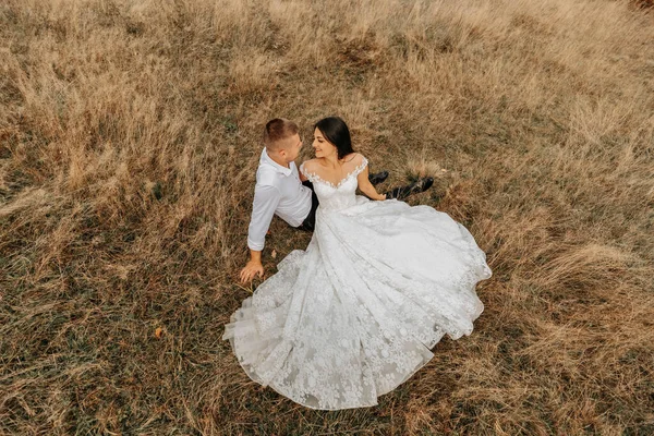 花嫁と新郎は 乾燥した草の上に横たわっていると抱擁 白いウェディングドレスの女性 美しい秋の結婚式の写真 — ストック写真