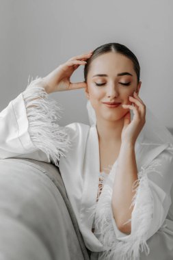 Güzel gelinin portresi, şık saç stili ve beyaz bornozlu, gözleri kapalı güzel bir kız.