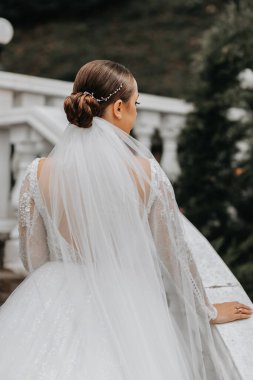 Gelinin şık bir görüntüsü, omuzları açık bir gelinlik. Gelin, arkası dönük, bahçedeki merdivenlerden damatına tırmanır..