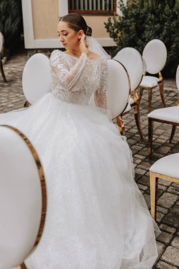 Uzun trenli bir gelin düğün töreninden sonra altın kenarlı beyaz sandalyelerde oturur ve poz verir.