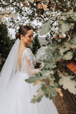 Doğada güzel bir gelin, yeşillikte elinde büyük bir buket çigila ile duruyor. Genç bir gelinin yakın plan düğün portresi. Düğün fotoğrafçılığı.