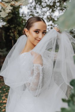 Doğada elinde peçeyle güzel bir gelin duruyor. Genç bir gelinin yakın plan düğün portresi. Düğün fotoğrafçılığı.