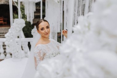 Beyaz çiçeklerle süslenmiş düğün kemerinin yanındaki parkta beyaz elbiseli tatlı esmer gelin. Yeni evlilerin düğün portresi..