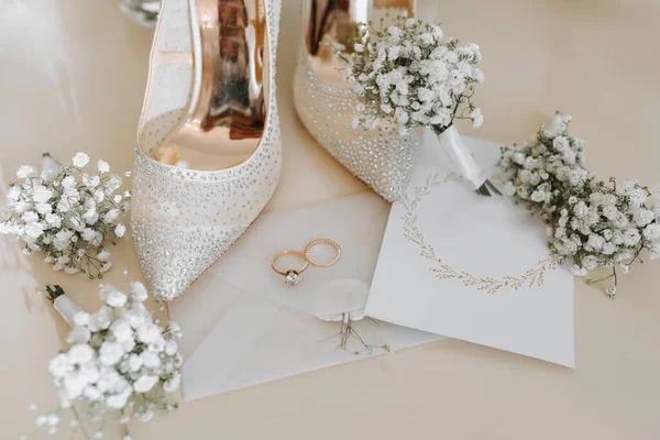 新娘和新郎的婚戒 婚戒上有一束束白花 两只漂亮的金戒指男人和女人的带装饰品的戒指 女式高跟鞋 案文的位置 — 图库照片