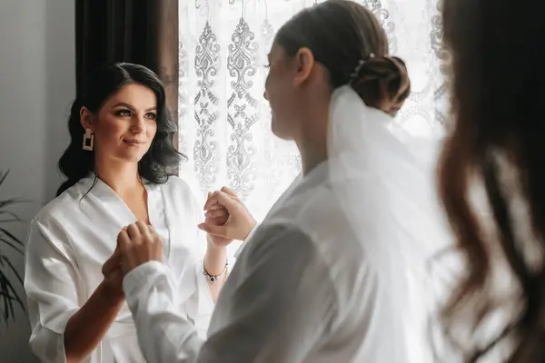 Girlfriends support the bride on her wedding day by holding hands in matching white robes