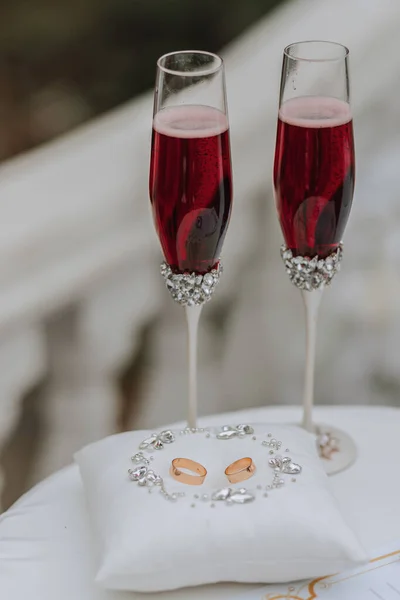 在枕头上挂着金戒指 上面镶嵌着银珠宝石 在附近挂着红色香槟酒的婚纱 为婚礼做准备 — 图库照片