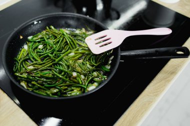 cooking greens, asparagus, garlic bunches, on a black pan and an electric stove, close-up