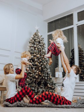 Cheerful and happy family with Christmas gifts near the Christmas tree in matching pajamas. Children are having fun. Loving family with gifts in the room.