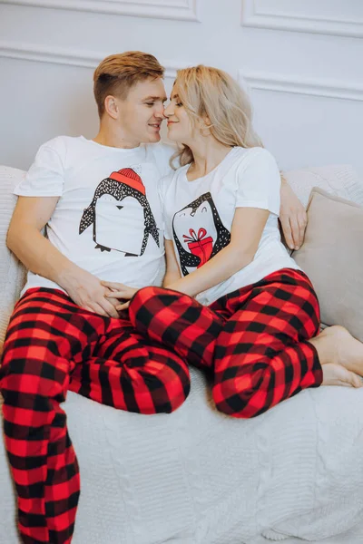 Cheerful and happy couple in matching pajamas lying on sofa. A loving family. The concept of New Year\'s holidays