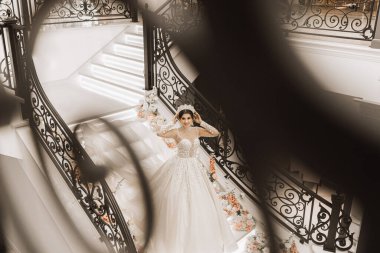 Gelinlik giymiş güzel bir gelin uzun trenle merdivenlerde duruyor çiçeklerle süslenmiş, yukarıdan çekilmiş bir fotoğraf.