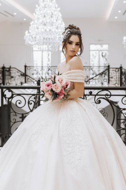 Güzel bir saç stili ve makyajı olan, elinde bir buket gülle lüks bir gelinlik içinde genç bir kız.