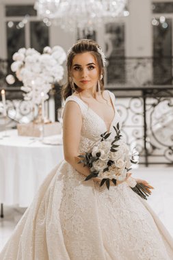 Elinde bir buket gülle gelinlik giymiş bir kızın göz kamaştırıcı stüdyo fotoğrafı. Lüks bir iç mekan. Dikey fotoğraf.