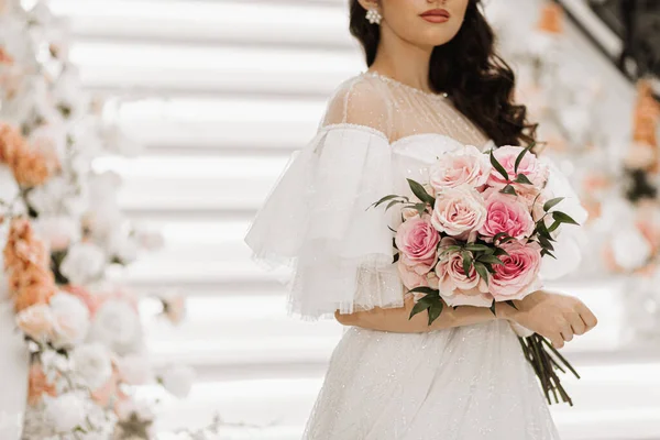 wedding bouquet of roses and greenery in the hands of a girl in a wedding dress