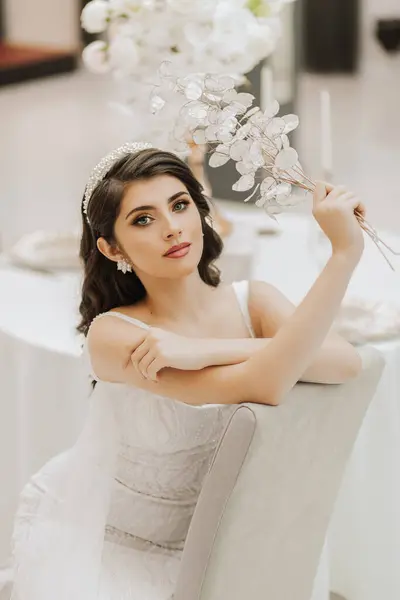 Portrait of a beautiful girl in a wedding dress. The bride in a luxurious dress, sitting on a chair. Vertical photo