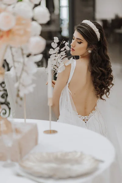 一个穿着敞着肩膀的婚纱的漂亮女孩的画像 照片来自后面 新娘穿着华丽的衣服 坐在椅子上 垂直照片 — 图库照片