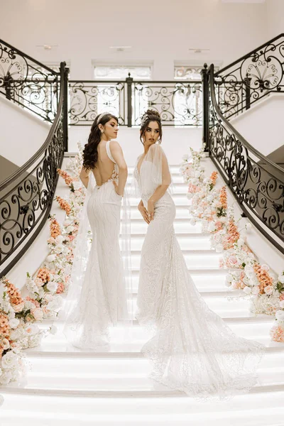 两个穿着婚纱的漂亮姑娘在一家装饰着鲜花的餐厅的楼梯上摆姿势 拍婚宴的照片 — 图库照片