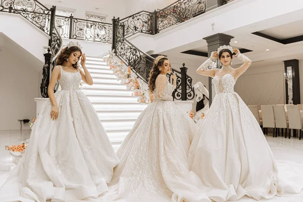 Три Красивые Девушки Роскошных Свадебных Платьях Длинными Поездами Позируют Зале — стоковое фото