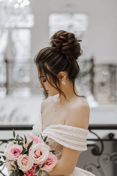 一个年轻姑娘 留着漂亮的发型 穿着华丽的婚纱 手里拿着一束玫瑰 — 图库照片