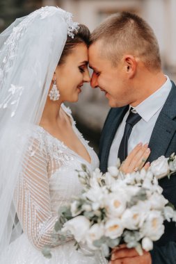 Düğün portresi. Uzun elbiseli esmer bir gelin ve klasik takım elbiseli bir damat bir gölün ve şatonun arka planında birbirlerine sarılıyorlar..