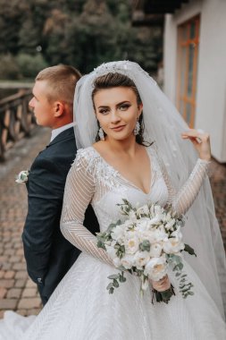 Düğün portresi. Uzun elbiseli esmer bir gelin damadının önünde bir buketle bir gölün ve bir kalenin arka planında duruyor..